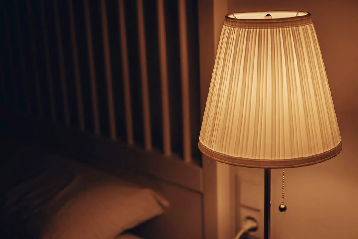 A warm bedside lamp switched on next to a bed in a dark room, the kind of low light used for nighttime bathroom trips