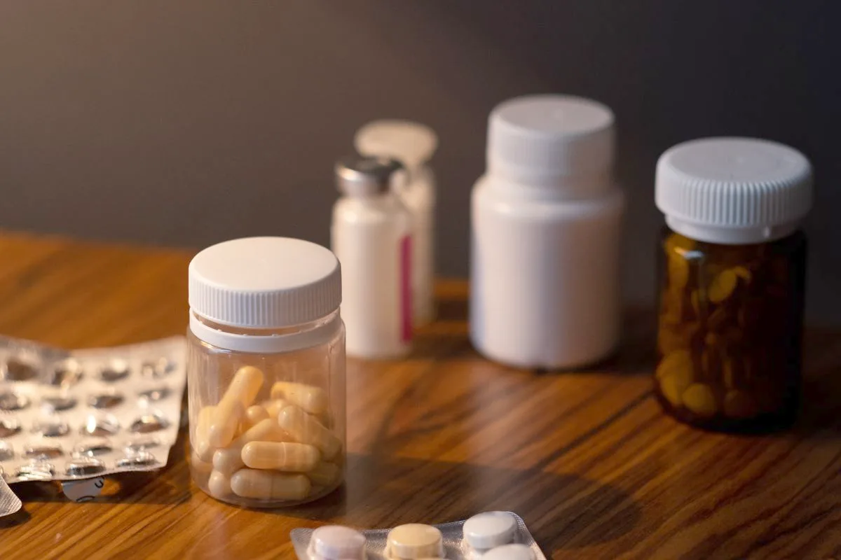Several unlabelled white supplement bottles and blister packs of capsules arranged on a dark wooden table